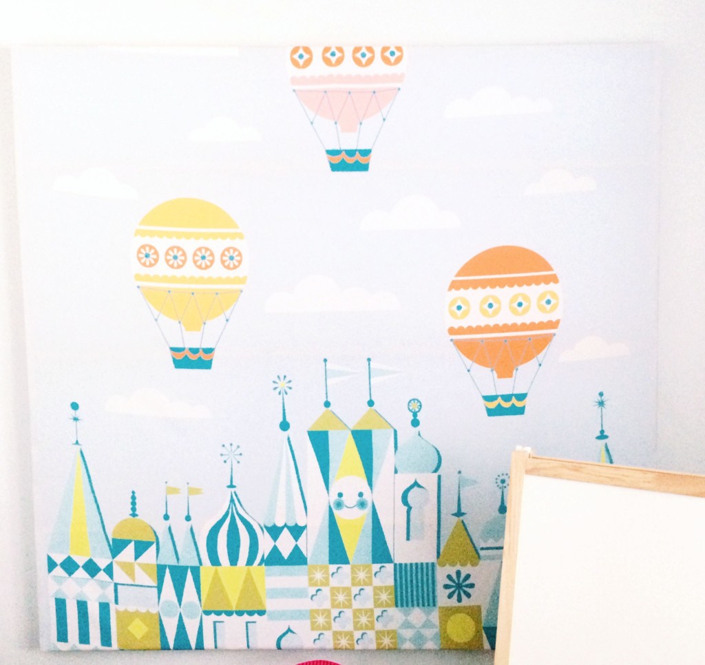 A DIY piece of canvas art displaying a cartoony version of three balloons and a pointed building tops.