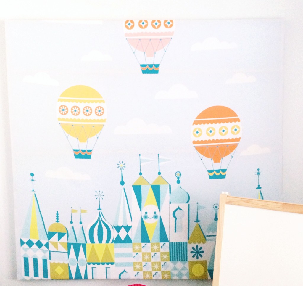 A DIY piece of canvas art displaying a cartoony version of three balloons and a pointed building tops.